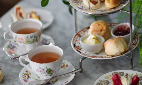 Cake stand filled with sandwiches, scones and cakes with cups and saucers with tea in them